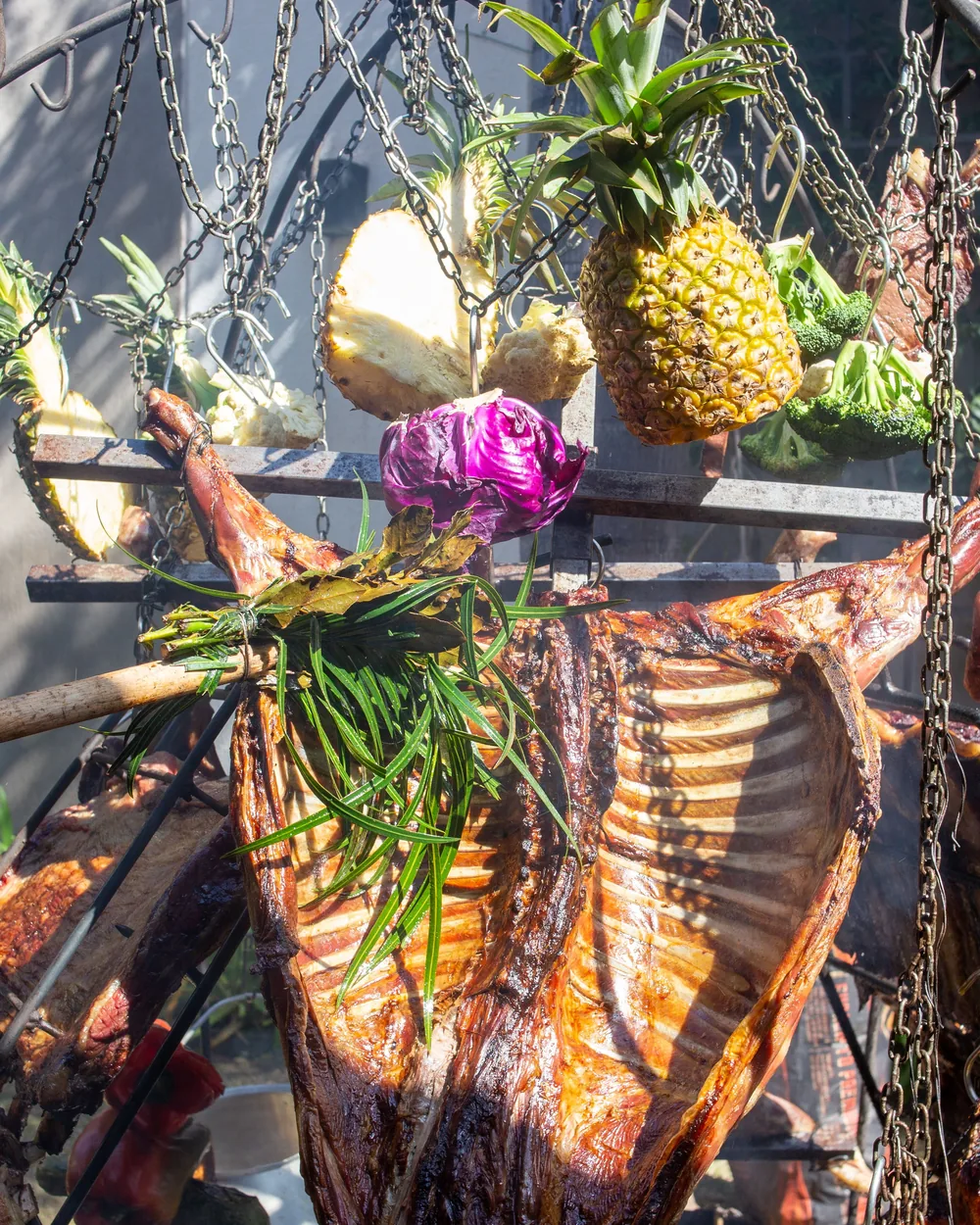 A whole roasted pig and grilled meats hanging on chains over a fire, garnished with pineapple and vegetables (representative photograph of a Polynesian-style feast, not the Chief's Luau buffet itself)