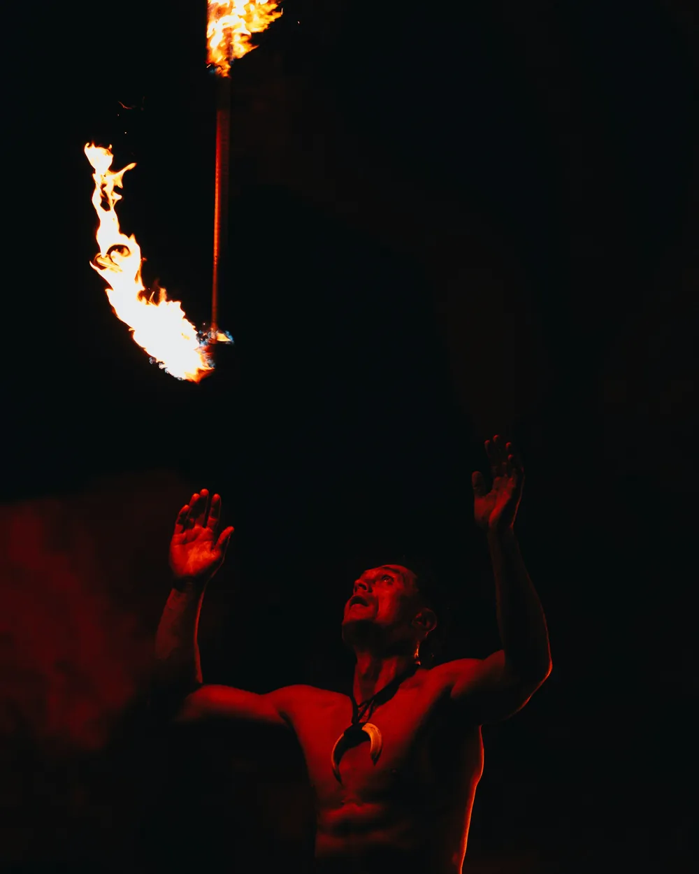 A Polynesian fire-knife performer holding a lit torch overhead against a dark night sky (representative photograph, not Chief's Luau)